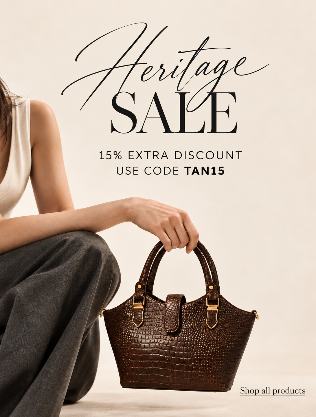 A woman in a white sleeveless top and dark gray pants sits beside a brown crocodile-embossed handbag, with large sale text reading 'Heritage SALE' and '15% EXTRA DISCOUNT USE CODE TAN15' on a warm beige background.